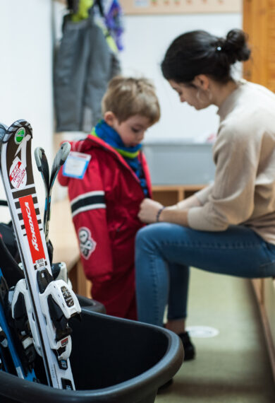 Educatrice qui ferme la veste d'un enfant avec son cours de ski à la Maison des Enfants Saint François Longchamp